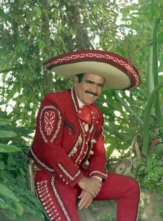 a man wearing a sombrero and sitting on a rock in front of trees