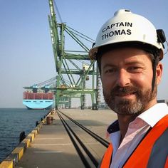 a man wearing a hard hat and safety vest standing in front of a large cargo ship