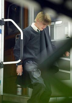 a young man wearing a sweater and tie climbing up the side of a train car