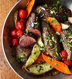 a pan filled with meat and vegetables on top of a wooden table next to utensils