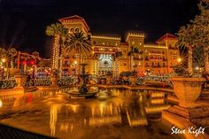 a fountain in front of a large building with christmas lights on the windows and trees around it