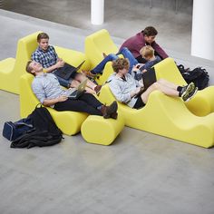 four people sitting on yellow couches with laptops and backpacks in the middle