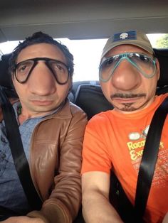 two men sitting in the back seat of a car wearing goggles and driving glasses