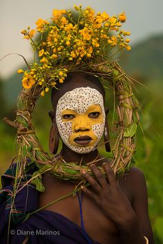 a woman with yellow face paint and flowers on her head is standing in a field