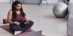 a woman sitting on a yoga mat using her laptop