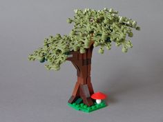 a lego model of a tree with green leaves and mushrooms on the ground, in front of a gray background