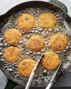 some food is cooking in a pan with water on the stove top and silver spoons next to it