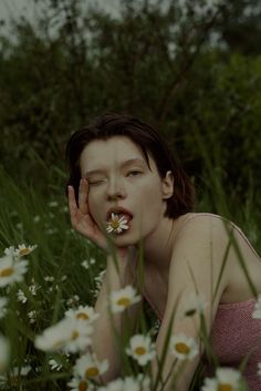 a woman laying in the grass with daisies on her nose and hands to her face