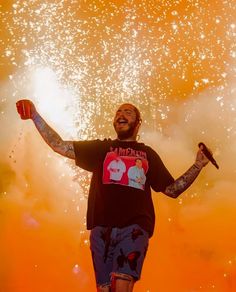 a man standing on top of a stage with his arms in the air and fireworks behind him