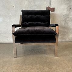 a black velvet chair with chrome frame and footrests in front of a concrete wall