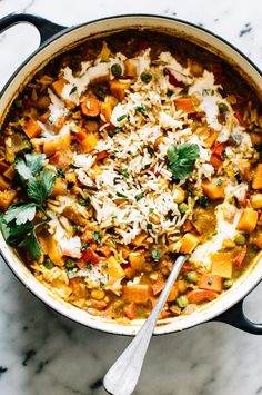 a large pot filled with lots of food on top of a marble countertop next to a spoon