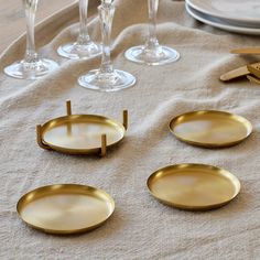 gold plates and utensils are arranged on a linen tablecloth with wine glasses in the background