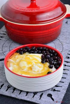 a red casserole dish with blueberries and cheese in it on a table