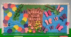 the bulletin board is decorated with paper butterflies and flowers, which read spread your wings