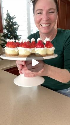 a woman is holding a plate with cupcakes and strawberries on it in the kitchen