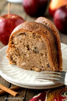 a piece of cake on a white plate with an apple in the background and cinnamon sticks