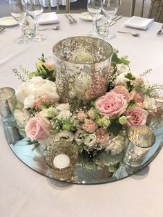 the centerpiece is surrounded by flowers, candles and silverware on a table with white linens