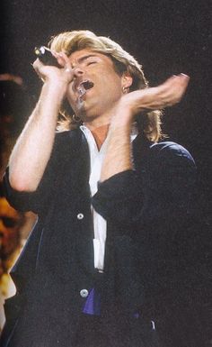 a man holding a microphone in his right hand and singing into the microphone with both hands