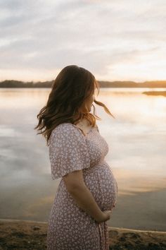 a pregnant woman standing by the water at sunset