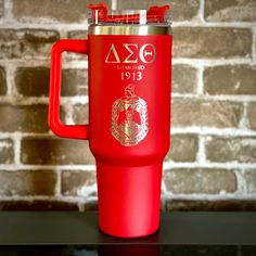 a red travel mug sitting on top of a black table next to a brick wall