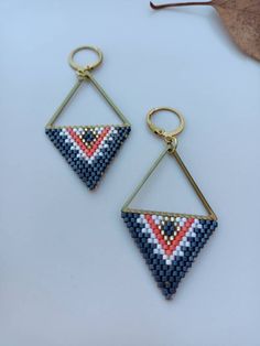 two triangle shaped beaded earrings hanging from gold hooks on a white surface with leaves