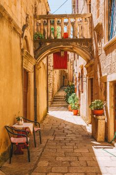 an alley way with tables and chairs on either side, surrounded by stone buildings in the background