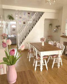 a dining room table and chairs with pink flowers in a vase on the floor next to it