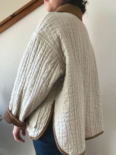 a woman standing in front of a wall with her back turned to the camera, wearing a sweater and jeans