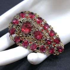 *Description: This is a beautiful red rhinestone dress clip from around the 1920s.  The antique gold tone is filigree with several sizes of red faceted rhinestones.  The dress clip is perfect to wear when you do not want to have a pin stuck through the material.  There are small sharp points inside the dress clip to hold the pin in place on the edge of a neckline, jacket or other areas where you want a little sparkle.  They are also placed on a belt or bags. This would be a great addition to you Vintage Red Jewelry With Rhinestones, Antique Red Wedding Brooch, Vintage Red Wedding Brooches, Red Rhinestone Brooches For Wedding, Red Rhinestone Wedding Brooches, Vintage Red Rhinestone Jewelry, Vintage Red Brooches For Party, Red Rhinestone Dress, Dress Clips