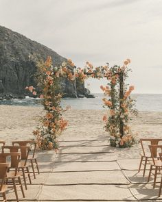 an outdoor ceremony set up on the beach with chairs and flowers in front of it