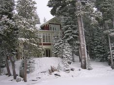 the house is surrounded by snow covered trees and evergreens in front of it,