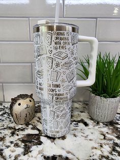 a stainless steel travel mug sitting on top of a counter next to a potted plant