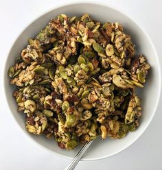 a bowl filled with nuts and raisins on top of a white table next to a spoon