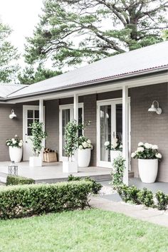 two large white planters sitting on the front porch of a gray house with windows