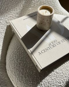 a book with a cup sitting on top of it next to a white couch cushion