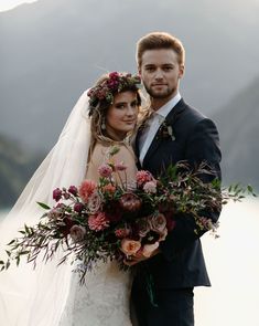 a bride and groom standing next to each other in front of the mountains with their bouquets