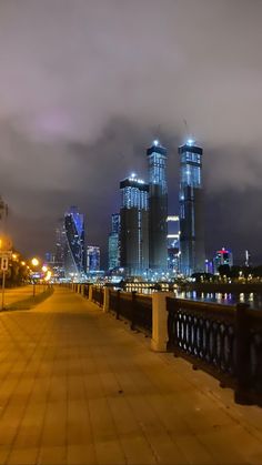 the city skyline is lit up at night with lights reflecting in the water and clouds