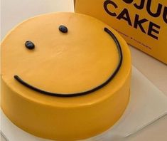 a yellow smiley face cake sitting on top of a table next to a sign that says jujuu cake