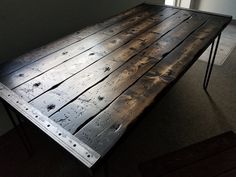 a table made out of wood with metal legs on the top and bottom, sitting in front of a window