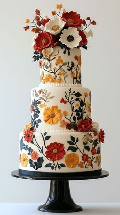 a multi - tiered cake decorated with flowers on a black stand against a white wall