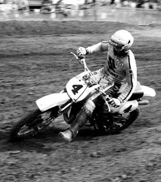 a man riding on the back of a dirt bike down a race track in black and white