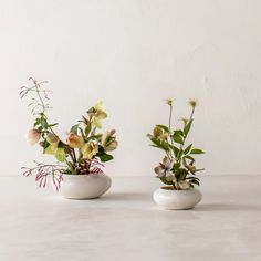 two white vases filled with flowers on top of a table