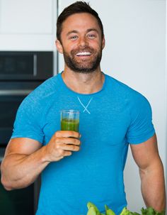 a man in a blue shirt holding a glass of green juice