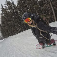 a man riding a snowboard down the side of a snow covered slope with trees in the background