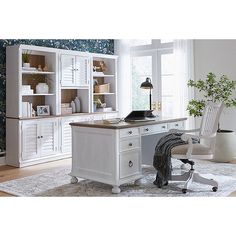 a white desk sitting in front of a window next to a chair and bookshelf