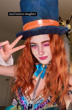 a woman with red hair wearing a blue top hat and holding up her peace sign