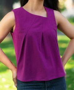 a woman standing in the grass with her hands on her hips, wearing a purple top