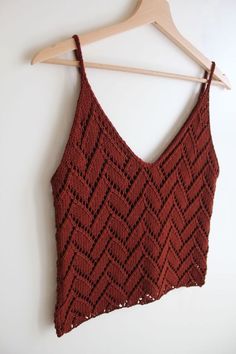 a crocheted crop top hanging on a hanger next to a white wall