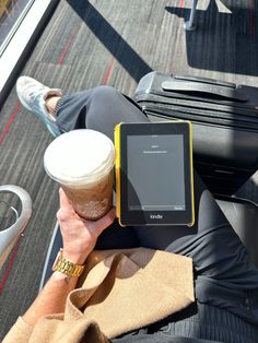 a person sitting on a bench with an electronic device in their hand and a cup of coffee next to them