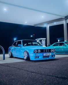 two cars parked next to each other in a parking lot at night with lights on